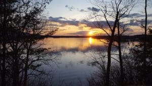 Sunset over a calm lake with trees.