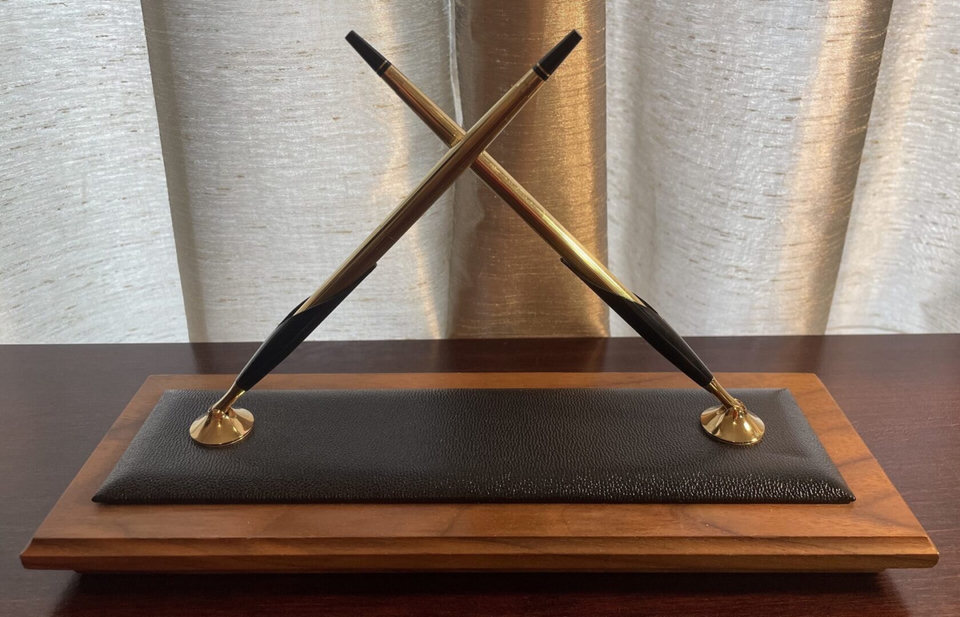 Crossed pens on a wooden display stand.