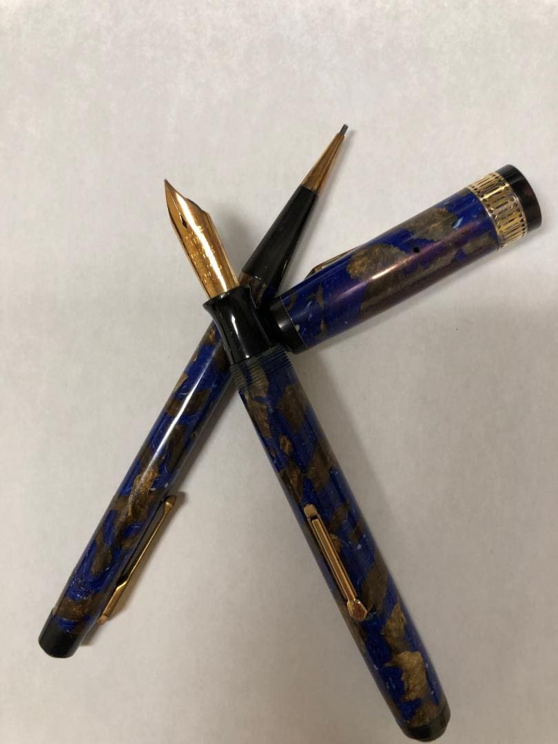 Two blue and gold fountain pens crossed on a white surface.